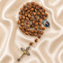 A wooden beads rosary, a medallion, and a crucifix with gold and silver details, arranged on a beige fabric background.