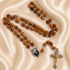 A wooden rosary with oval beads, silver-toned chain links, an oval medallion, and a crucifix pendant, on draped satin fabric.