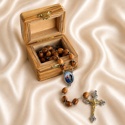 A wooden rosary and a gold- and silver-crucifix, displayed beside an open wooden box on draped satin fabric.
