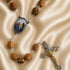 A rosary with wooden beads, an oval medallion with the Holy Family, a silver and gold tone crucifix, on a beige fabric background