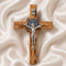 Handcrafted olive wood cross with St. Benedict medallion and silver crucifix on a white cloth