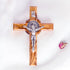 Frontal image of a handcrafted olive wood cross with St. Benedict medallion and silver-toned crucifix detail on a white background with petals.