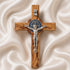 Handcrafted olive wood cross with St. Benedict medallion and silver crucifix on a white cloth