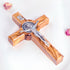 Handcrafted olive wood cross with St. Benedict medallion and silver-toned crucifix detail on a white background with petals.