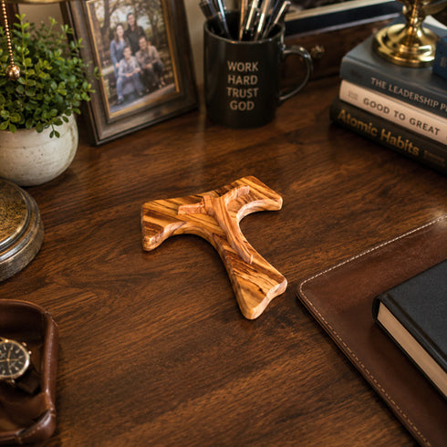Wooden Tau cross on a wooden desk with motivational items and decor.