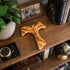 Wooden Tau cross on a wooden shelf with books, a clock, and a photo frame.
