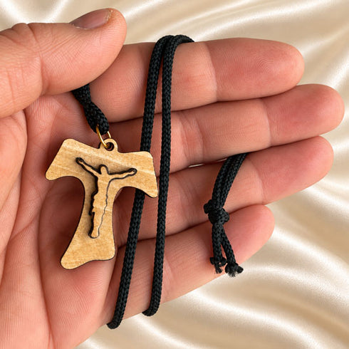Tau crucifix necklace close-up: olive wood pendant on black braided cord
