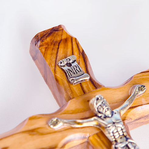 A detail of a handcrafted olive wood thorn cross with a crucifix, placed on a white surface.