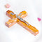 A handcrafted olive wood thorn cross with a crucifix, placed on a white surface with a few pink flowers scattered around.