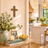 Decorative setup with books, flowers, and a cross on a wall in a home interior.