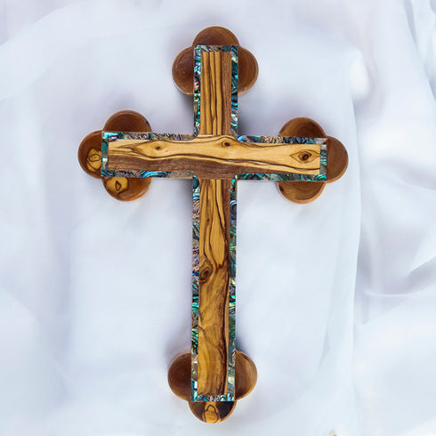A handcrafted olive wood Eastern cross with mother-of-pearl inlays. Set against a white fluffy background.
