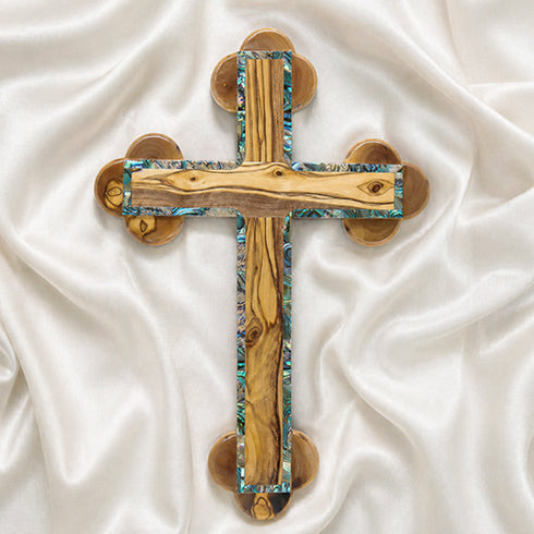 A handcrafted olive wood Eastern cross with mother-of-pearl inlays. Set against a white fluffy background.