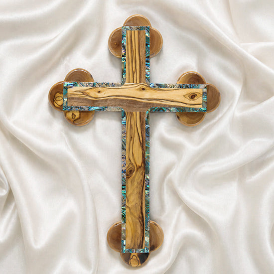 A handcrafted olive wood Eastern cross with mother-of-pearl inlays. Set against a white fluffy background.