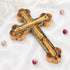 A handcrafted olive wood budded cross with green mother-of-pearl inlay, featuring the Twelve Stations of the Cross engraved on the back, placed on a white fabric surface.