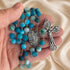 A close-up of a rosary held in a person's hand, featuring turquoise and light blue marbled beads.