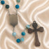 A rosary with turquoise and light blue beads, a silver-tone centerpiece, and a metal cross, on a satin fabric background.