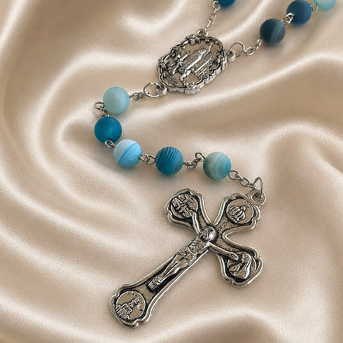 A rosary with blue and light blue marbled beads, metal crucifix on a beige satin fabric background.