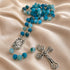 A turquoise and light blue rosary with metal links, a medallion, and a crucifix, on draped satin fabric.