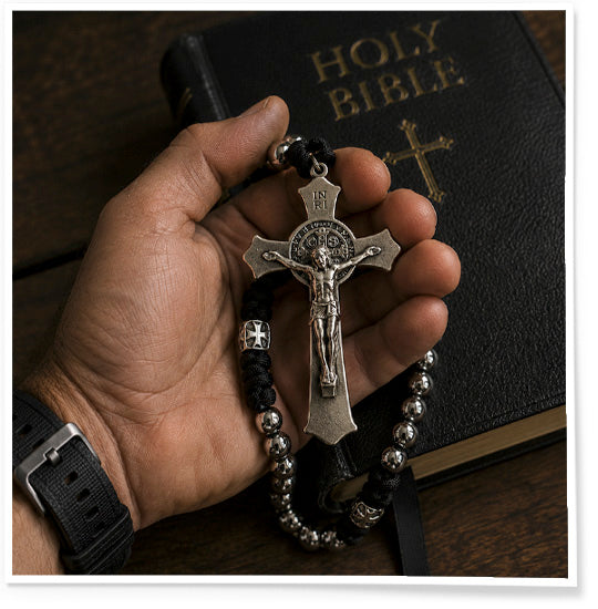 Hand holding a crucifix and rosary beads with a Holy Bible in the background