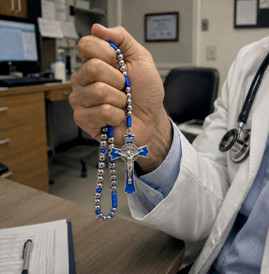 Person in a medical setting holding a rosary with blue and silver beads.