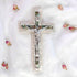 Frontal image of a classic olive wood Latin cross featuring silver crucifix and Mother of Pearl inlay detail, surrounded by soft rose petals on a clean white surface.