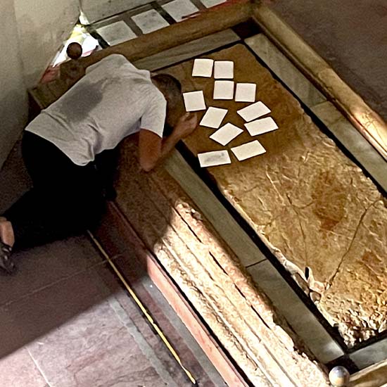 A person praying and placing a prayer notes on the Stone of Anointing inside the Church of the Holy Sepulchre.