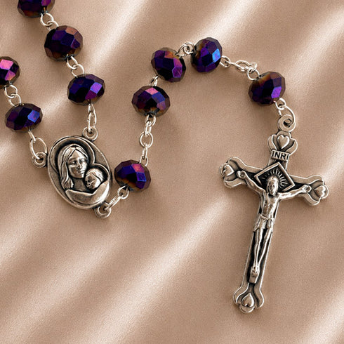 A rosary with purple beads and silver-tone metal links, a silver medallion of the Virgin Mary holding a baby and a detailed crucifix.