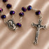 A rosary with purple beads and silver-tone metal links, a silver medallion of the Virgin Mary holding a baby and a detailed crucifix.