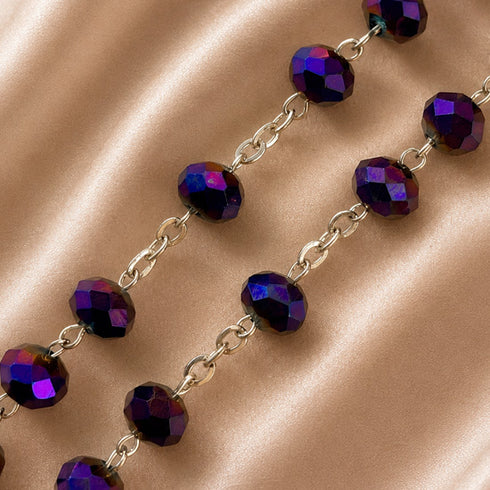 Faceted purple beads with an iridescent finish connected by silver-toned chains, on a champagne satin fabric.