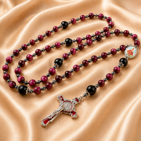 A rosary with red and black beads, a silver crucifix with red enamel, and a medal, on a beige satin fabric.