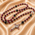 A rosary with red and black beads, a silver crucifix with red enamel, and a medal, on a beige satin fabric.