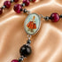 A close-up of rosary on satin fabric, red beads, silver spacers, a central oval medallion with Jesus in a red.