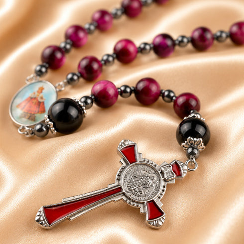 A close-up of a rosary with red and black beads, a silver crucifix with red enamel details, a medallion, on a beige satin.