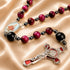A rosary with red and black beads, a oval saint medal, and a silver-tone crucifix, on a beige background.