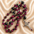 A gothic-style rosary with red and black beads, a silver-toned crucifix and a medallion, on a satin fabric.