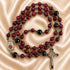A Catholic rosary with red and black beads, a silver-tone crucifix, and a small oval medallion on a beige fabric background.