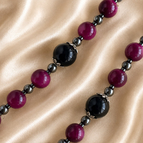 A close-up of a large glossy black round beads and smaller dark red beads separated by dark gray beads, on a satin fabric.