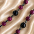 A close-up of a large glossy black round beads and smaller dark red beads separated by dark gray beads, on a satin fabric.
