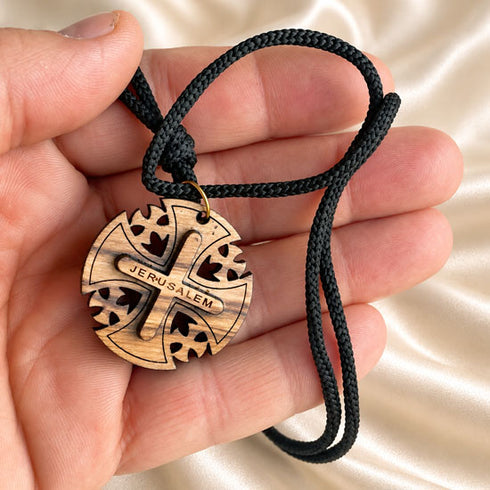 Round wooden Jerusalem cross pendant necklace held in hand on black braided cord
