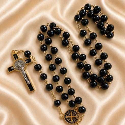 A black and gold rosary, a gold crucifix with black enamel, and a gold centerpiece medallion, on a satin fabric background.