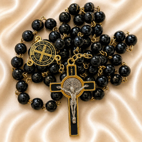 Black bead rosary with gold-plated chain and a gold and silver crucifix, on a beige satin background.