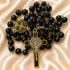 Black bead rosary with gold-plated chain and a gold and silver crucifix, on a beige satin background.