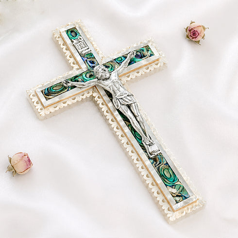 Image of a classic olive wood Latin cross featuring silver crucifix and Mother of Pearl inlay, surrounded by soft rose petals on a clean white surface.
