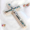 Image of a classic olive wood Latin cross featuring silver crucifix and Mother of Pearl inlay, surrounded by soft rose petals on a clean white surface.