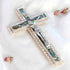 Image of a classic olive wood Latin cross featuring silver crucifix and Mother of Pearl inlay, surrounded by soft rose petals on a clean white surface.