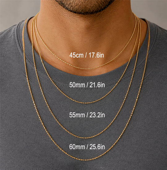 Gold necklaces of different lengths displayed on a man wearing a gray shirt.
