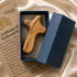 A wooden comfort cross, in an open dark blue box next to its certificate of authenticity on a beige satin background.