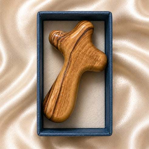Olive wood comfort cross resting in an open blue gift box on ivory satin background.
