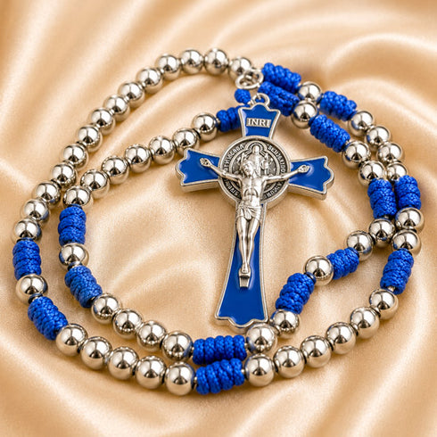 A silver beaded rosary with blue cord, a crucifix pendant, displayed on a satin fabric background.