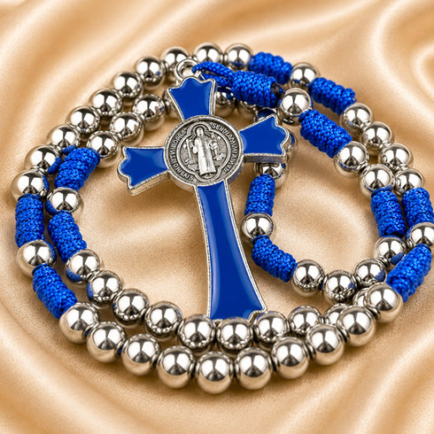 A silver beaded rosary with a blue cord and cross, on a beige satin fabric background.